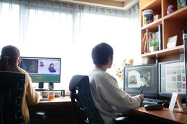 明るい窓を背にデスクに向かう2人のスタッフが、3Dアニメーション制作ソフトを映した2台のモニターを前に作業している
