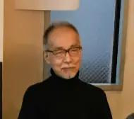 眼鏡をかけた白髪まじりの男性が、黒いタートルネックを着て正面を向いている上半身の写真